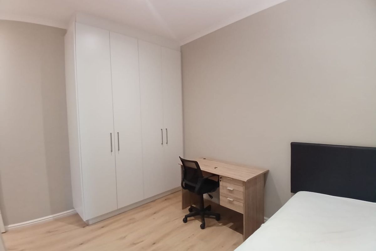 A clean, modern bedroom featuring light laminate flooring, neutral walls, and a large white built-in wardrobe with ample storage space.