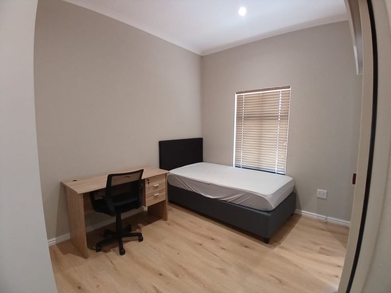 A clean, neutral-toned bedroom featuring light wood-look laminate flooring, modern venetian blinds, and recessed lighting, providing a functional and well-maintained living space.