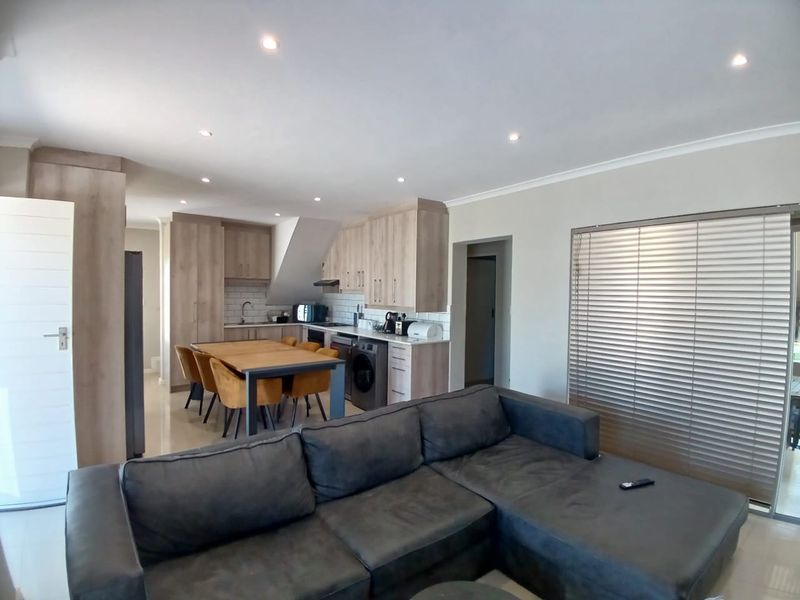 Modern open-plan living and kitchen area featuring light wood cabinetry, subway tile backsplash, recessed lighting, and tiled flooring throughout.