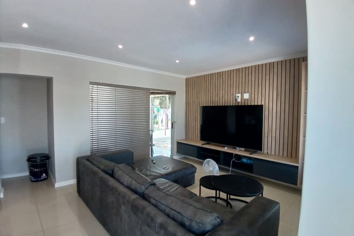 Modern living room featuring a stylish timber slat feature wall, built-in media cabinetry, recessed downlighting, and neutral tiled flooring.