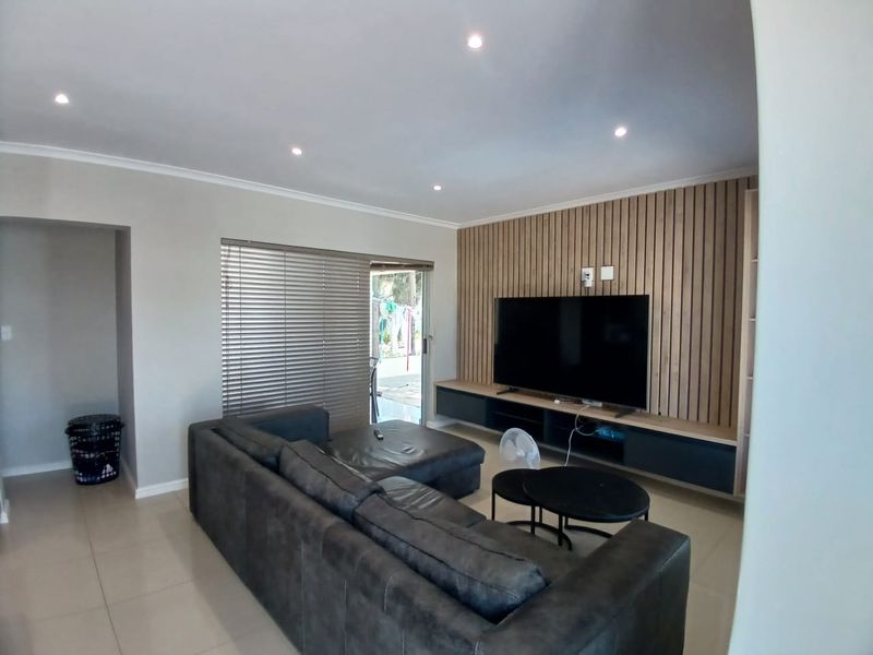 Modern living room featuring a stylish timber slat feature wall, built-in media cabinetry, recessed downlighting, and neutral tiled flooring.
