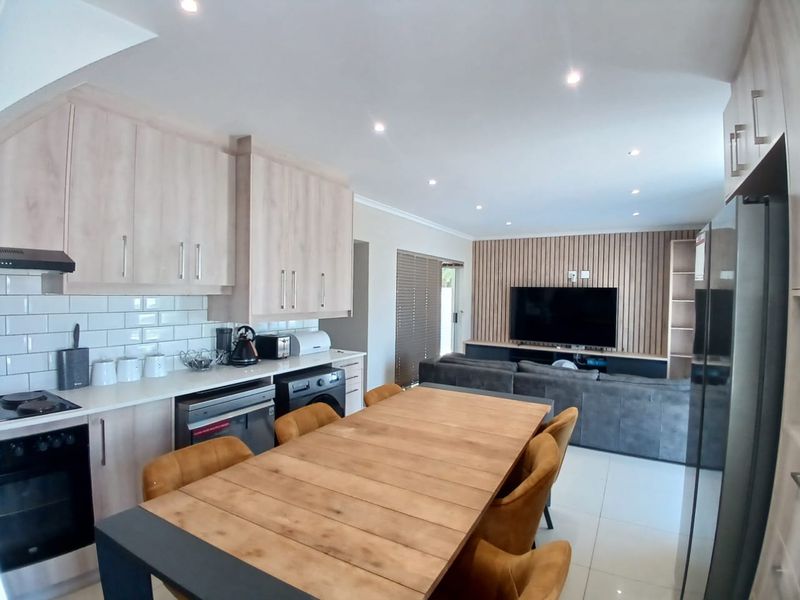 Modern open-plan living area featuring a contemporary kitchen with light wood cabinetry, subway tile backsplash, and a stylish slatted wood feature wall.