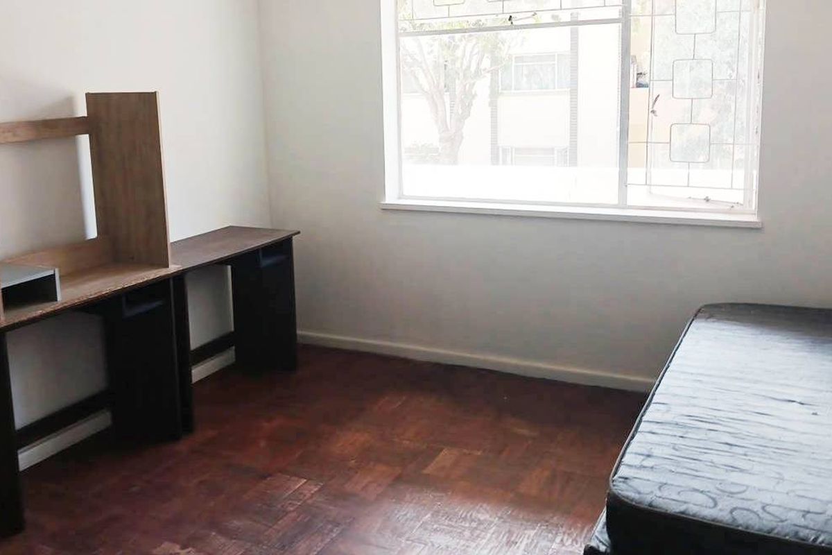A bedroom featuring parquet flooring and a window fitted with security bars, offering a functional space with potential for cosmetic updates.