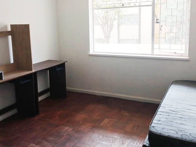 A bedroom featuring parquet flooring and a window fitted with security bars, offering a functional space with potential for cosmetic updates.
