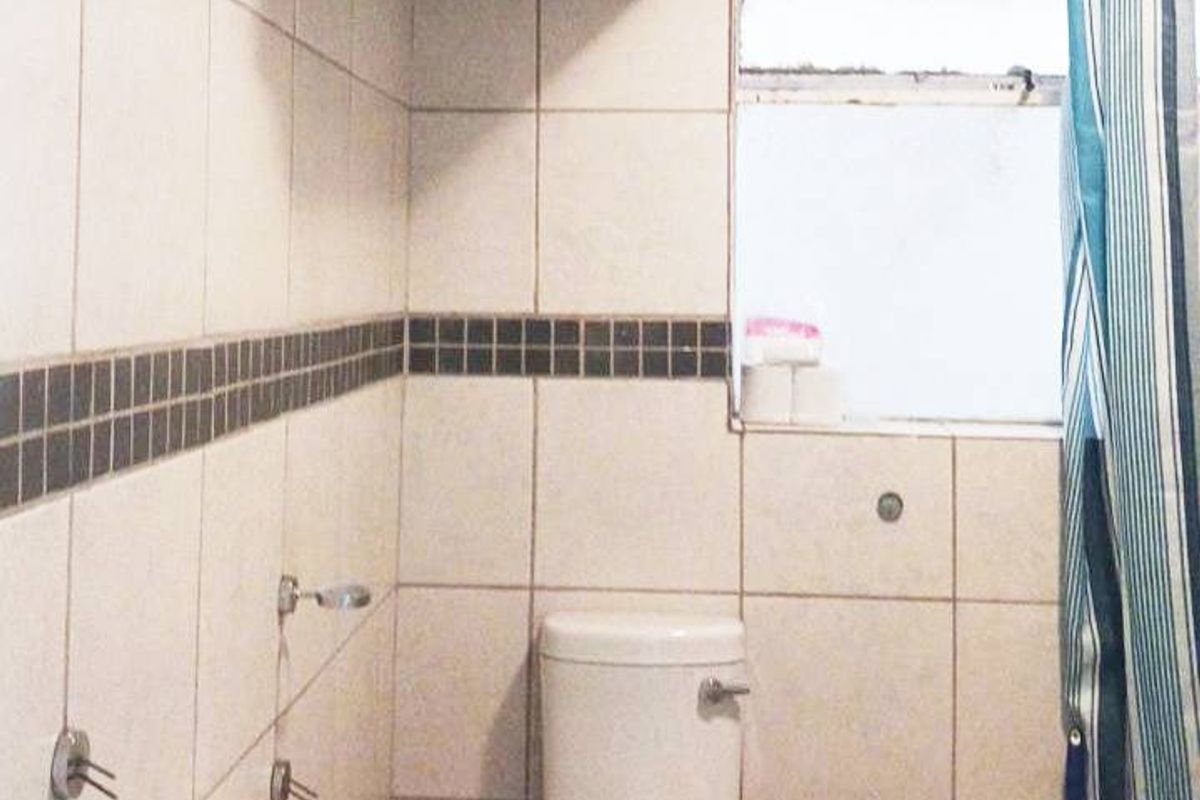 A compact bathroom featuring a pedestal basin, toilet, and shower area with tiled finishes and an overhead electric water heater.