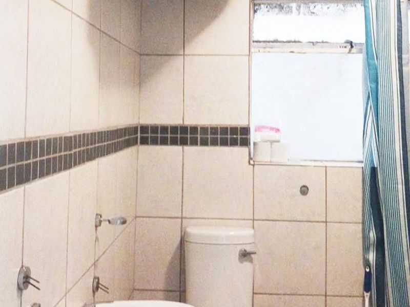 A compact bathroom featuring a pedestal basin, toilet, and shower area with tiled finishes and an overhead electric water heater.