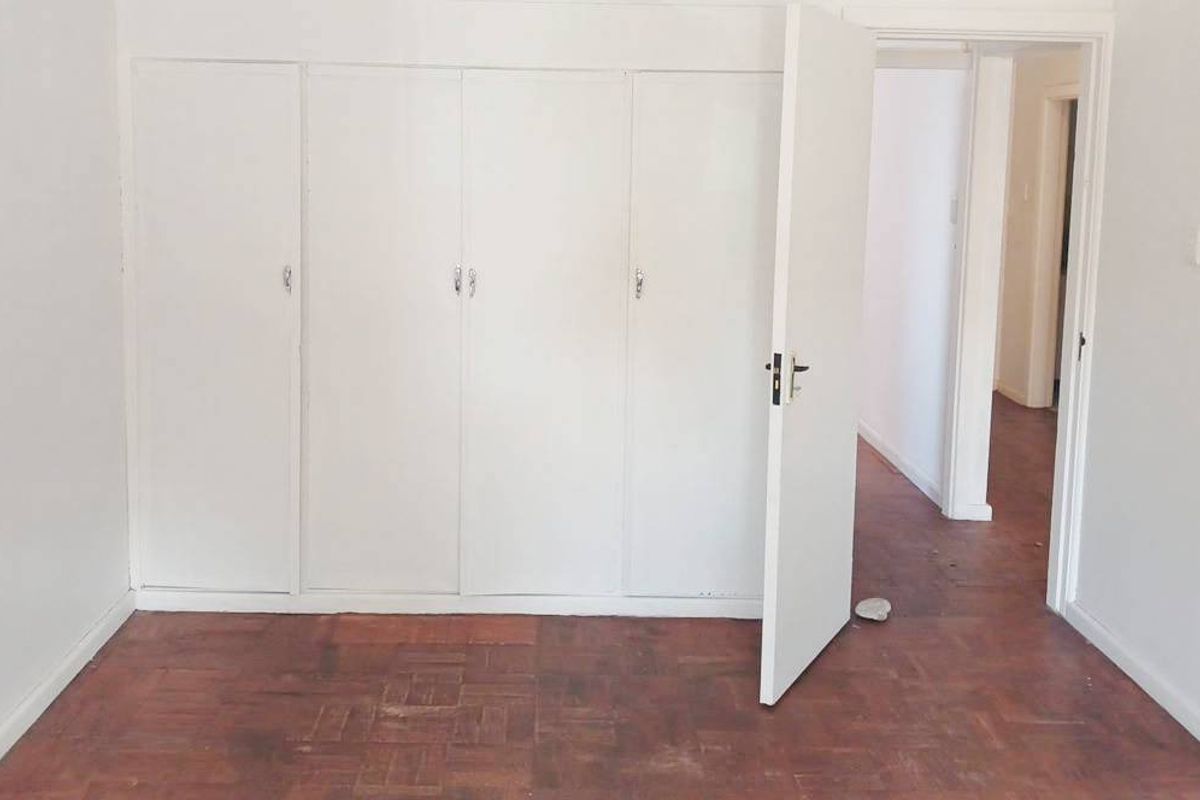 An empty bedroom featuring classic parquet flooring and white built-in cupboards, offering a blank canvas for renovation or interior design updates.
