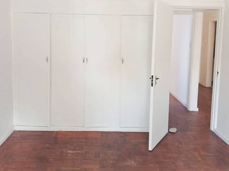 An empty bedroom featuring classic parquet flooring and white built-in cupboards, offering a blank canvas for renovation or interior design updates.