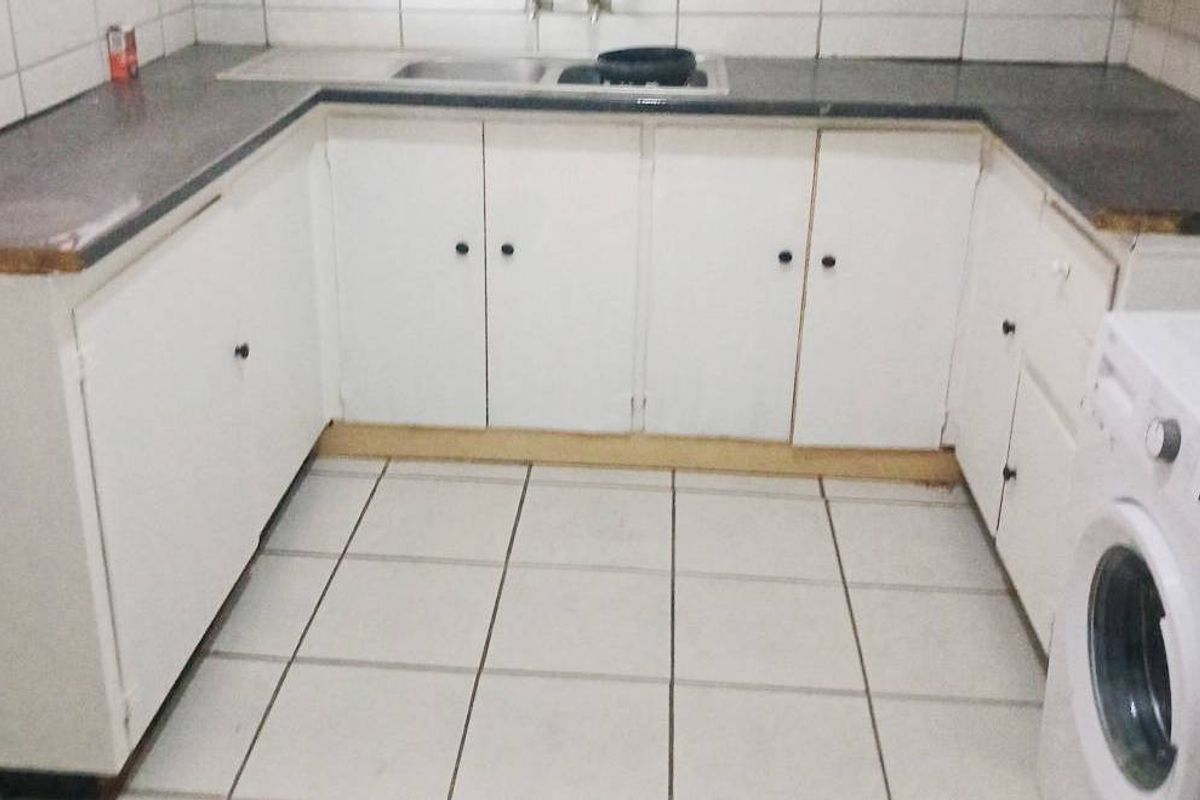 A functional kitchen featuring U-shaped white cabinetry, dark laminate countertops, a stainless steel sink, and tiled flooring with a dedicated laundry appliance space.