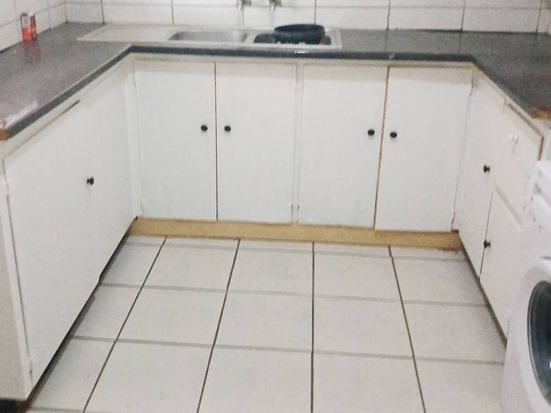 A functional kitchen featuring U-shaped white cabinetry, dark laminate countertops, a stainless steel sink, and tiled flooring with a dedicated laundry appliance space.