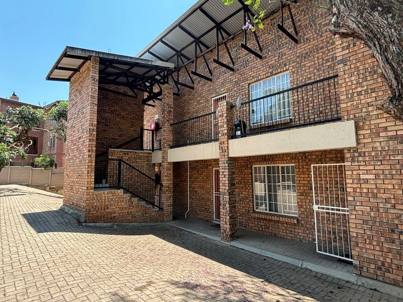 Exterior view of a multi-story apartment building featuring face brick construction, a metal roof, and paved driveway access.