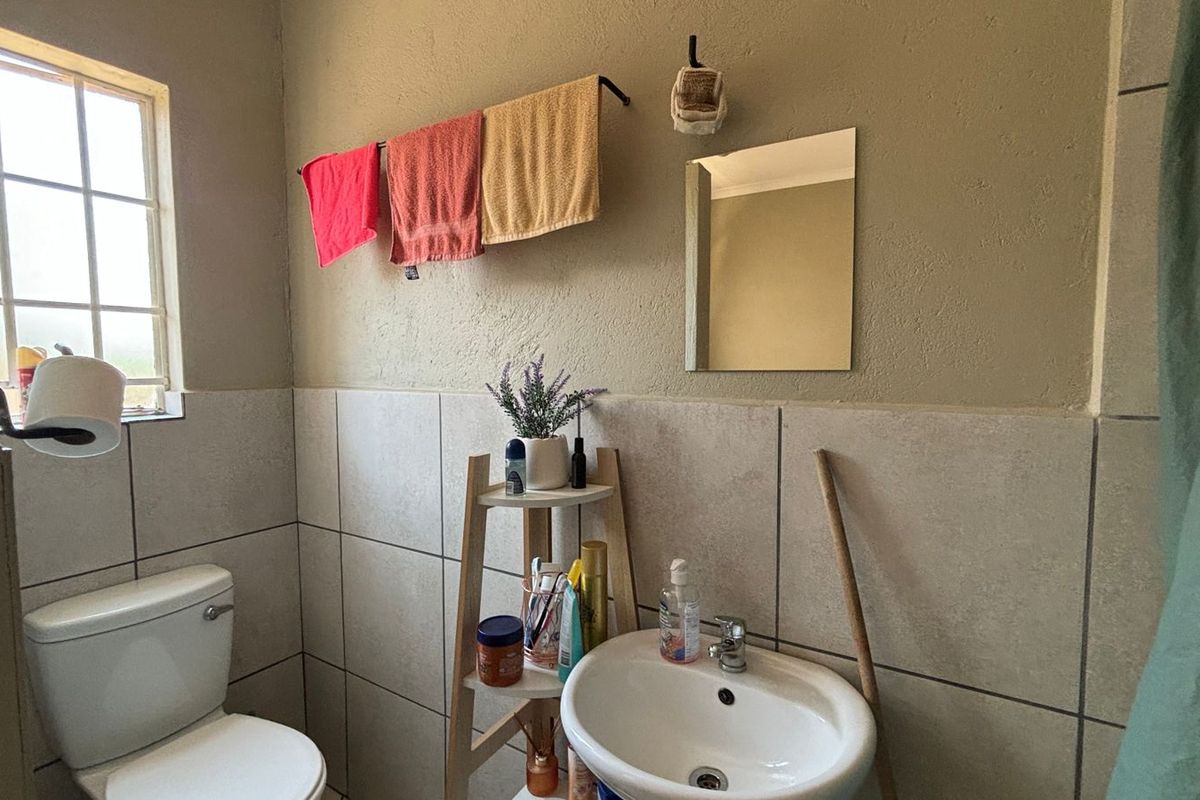 A functional bathroom featuring a pedestal washbasin, ceramic toilet, tiled wall finishes, and a wall-mounted mirror with natural light from a window.