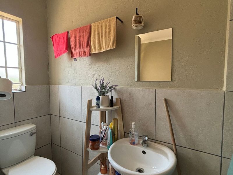 A functional bathroom featuring a pedestal washbasin, ceramic toilet, tiled wall finishes, and a wall-mounted mirror with natural light from a window.