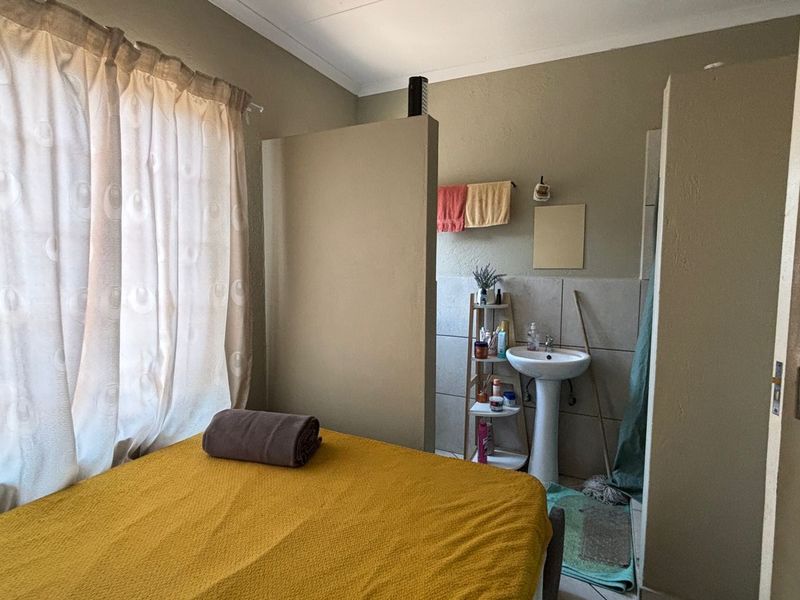 A bedroom featuring an open-plan layout with an integrated pedestal basin and tiled splashback area.