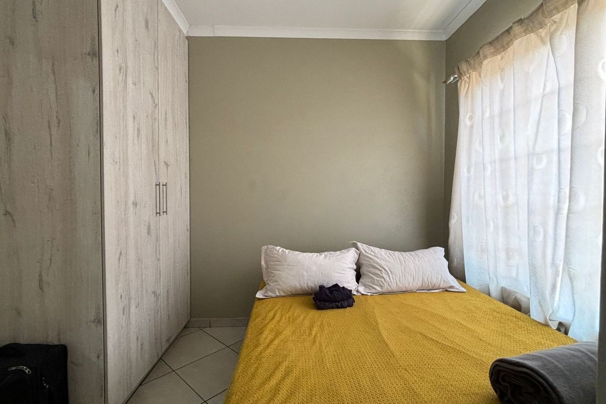 A compact bedroom featuring built-in cupboards, tiled flooring, and neutral wall tones, offering a functional space with natural light.