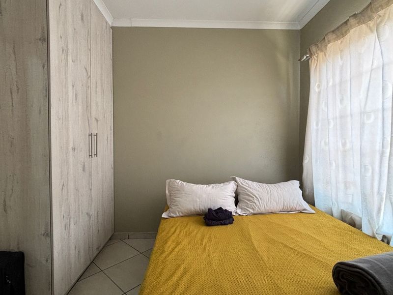 A compact bedroom featuring built-in cupboards, tiled flooring, and neutral wall tones, offering a functional space with natural light.