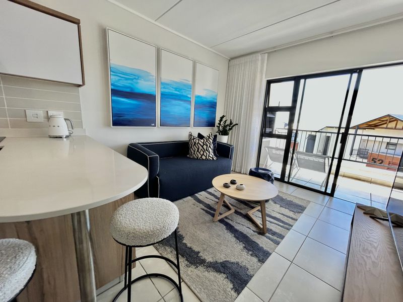 Modern open-plan living area featuring a breakfast bar, tiled flooring, and seamless access to a private balcony through large sliding glass doors.