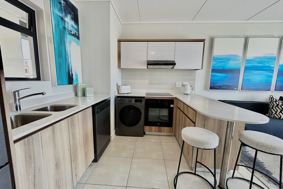 Modern kitchen featuring light wood-grain cabinetry, stone countertops, integrated appliances, and a functional breakfast bar with tiled flooring.