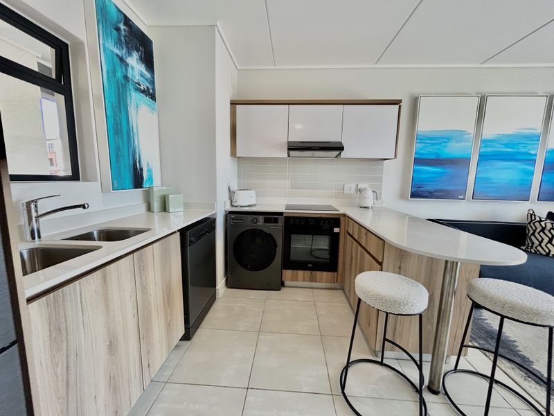 Modern kitchen featuring light wood-grain cabinetry, stone countertops, integrated appliances, and a functional breakfast bar with tiled flooring.
