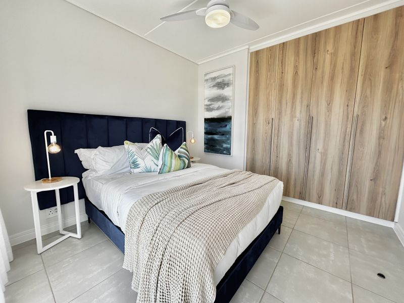 A modern bedroom featuring light-toned tiled flooring, a ceiling fan, and floor-to-ceiling wood-finish built-in cupboards.
