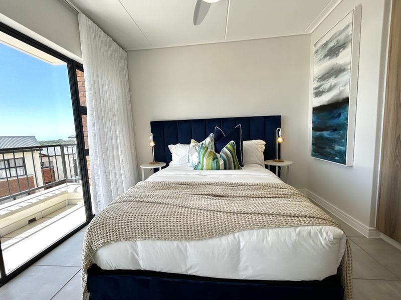 A modern, well-maintained bedroom featuring tiled flooring, a ceiling fan, and a large sliding glass door providing access to a private balcony.