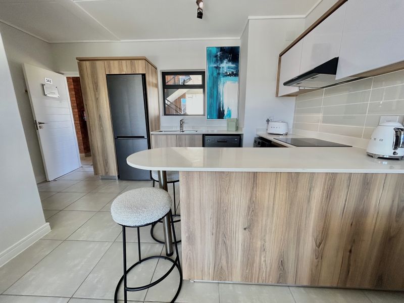 Modern kitchen featuring wood-grain cabinetry, stone countertops, a breakfast bar, integrated hob, and extractor fan, complemented by neutral tiled flooring.