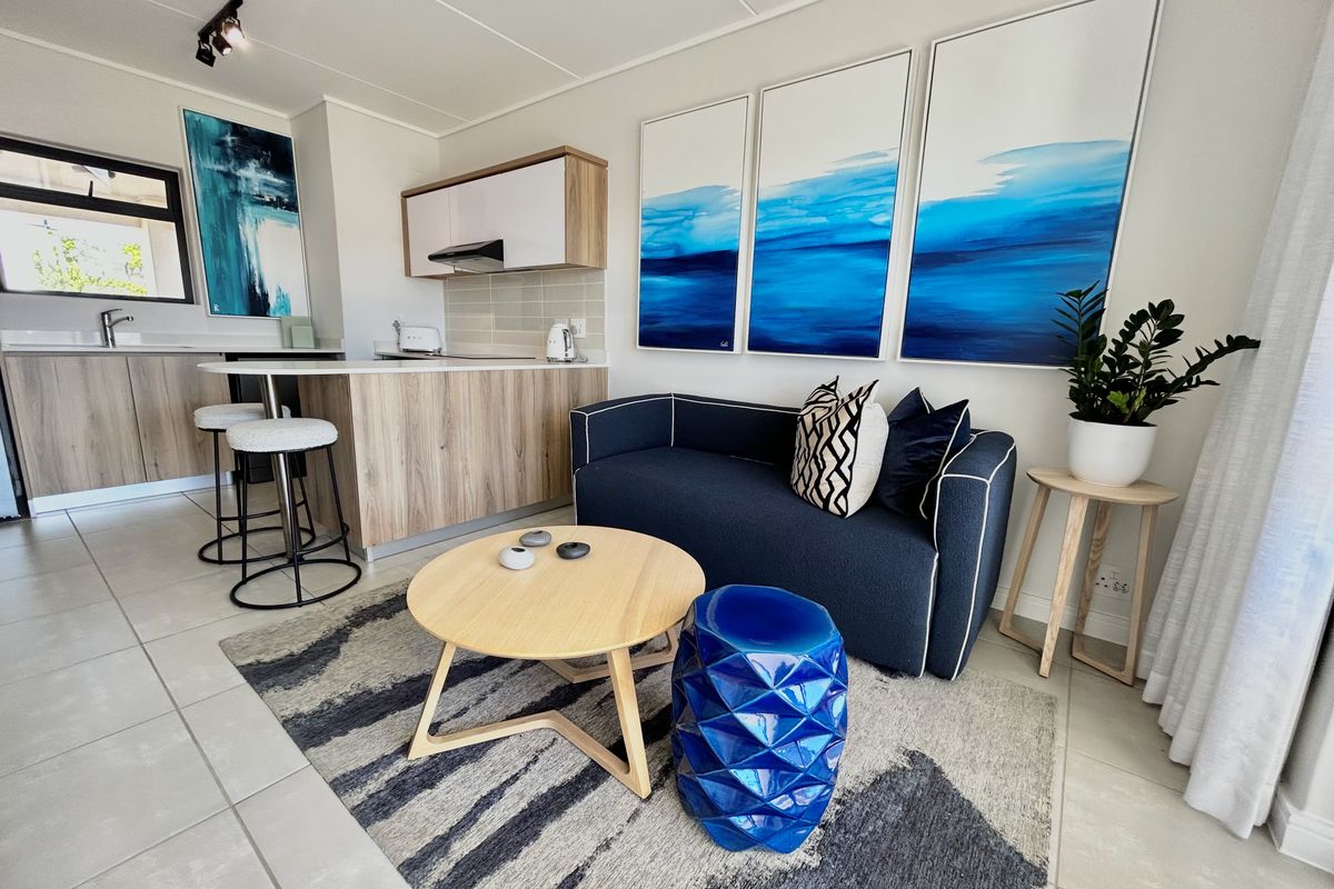 Modern open-plan living area featuring a compact kitchen with wood-finish cabinetry, a breakfast island, and neutral tiled flooring throughout the space.