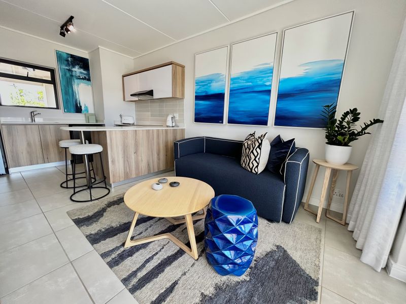 Modern open-plan living area featuring a compact kitchen with wood-finish cabinetry, a breakfast island, and neutral tiled flooring throughout the space.