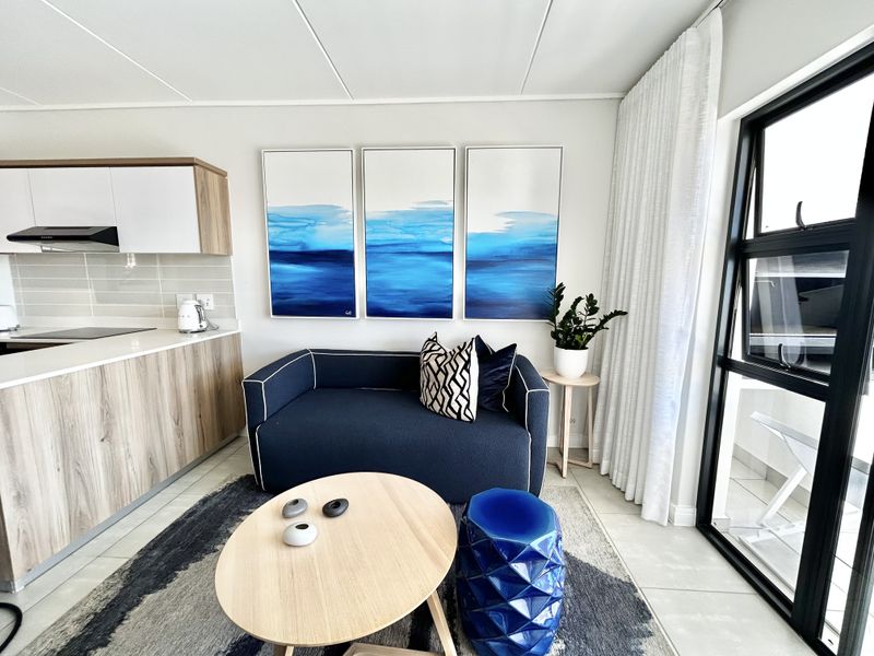Modern open-plan living area featuring a sleek kitchen with wood-grain cabinetry, tiled floors, and large glass doors leading to an outdoor space.