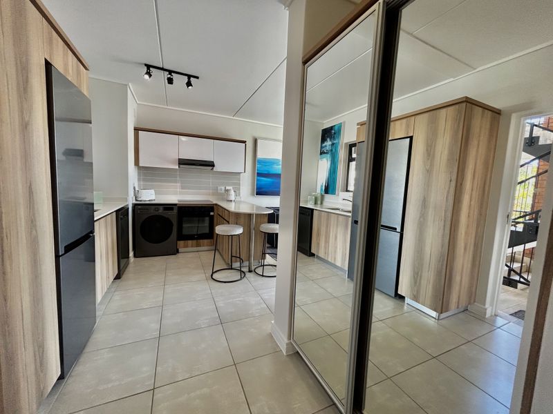 Modern kitchen featuring wood-finish cabinetry, tiled flooring, integrated appliances, and a breakfast bar, complemented by a large mirrored storage unit.