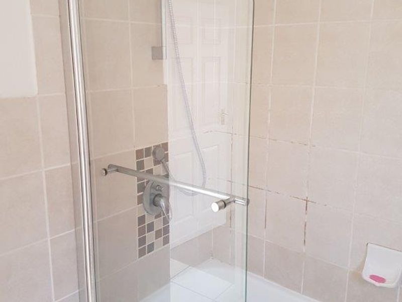 A functional bathroom featuring a bathtub with a glass shower screen, wall tiling with mosaic accents, and a standard shower mixer.