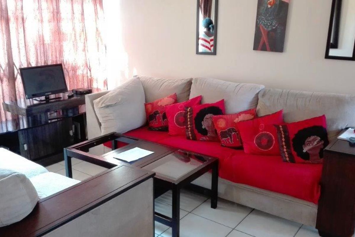 A living room area featuring tiled flooring and access to an outdoor space through a sliding door with a security gate.