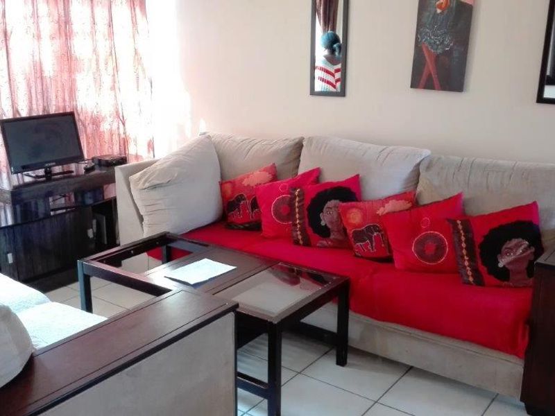 A living room area featuring tiled flooring and access to an outdoor space through a sliding door with a security gate.