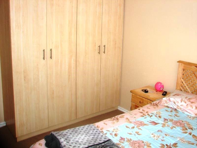 A bedroom featuring light wood-finish built-in wardrobes with modern metal handles.