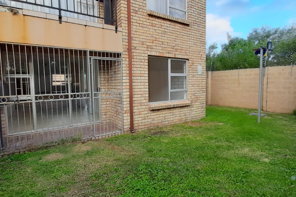 Rear view of a townhouse featuring a face brick facade, a small private lawn, and security features including a gate and electric fencing.