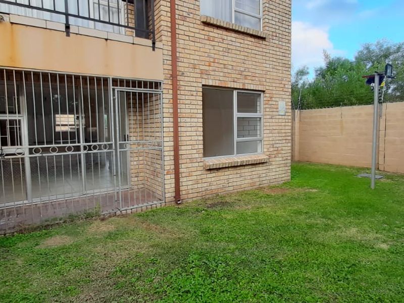 Rear view of a townhouse featuring a face brick facade, a small private lawn, and security features including a gate and electric fencing.