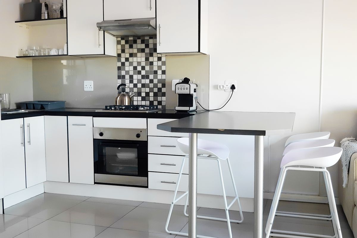 Modern kitchen featuring white cabinetry, black countertops, a built-in oven, stainless steel extractor fan, and a tiled backsplash with a breakfast bar area.