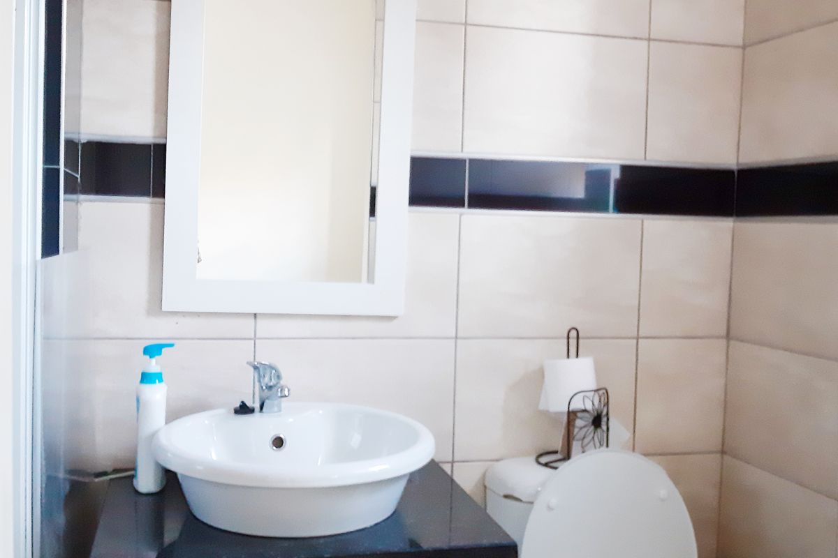 A compact bathroom featuring a white vessel sink on a dark vanity, a wall-mounted mirror, and a standard toilet with tiled walls.