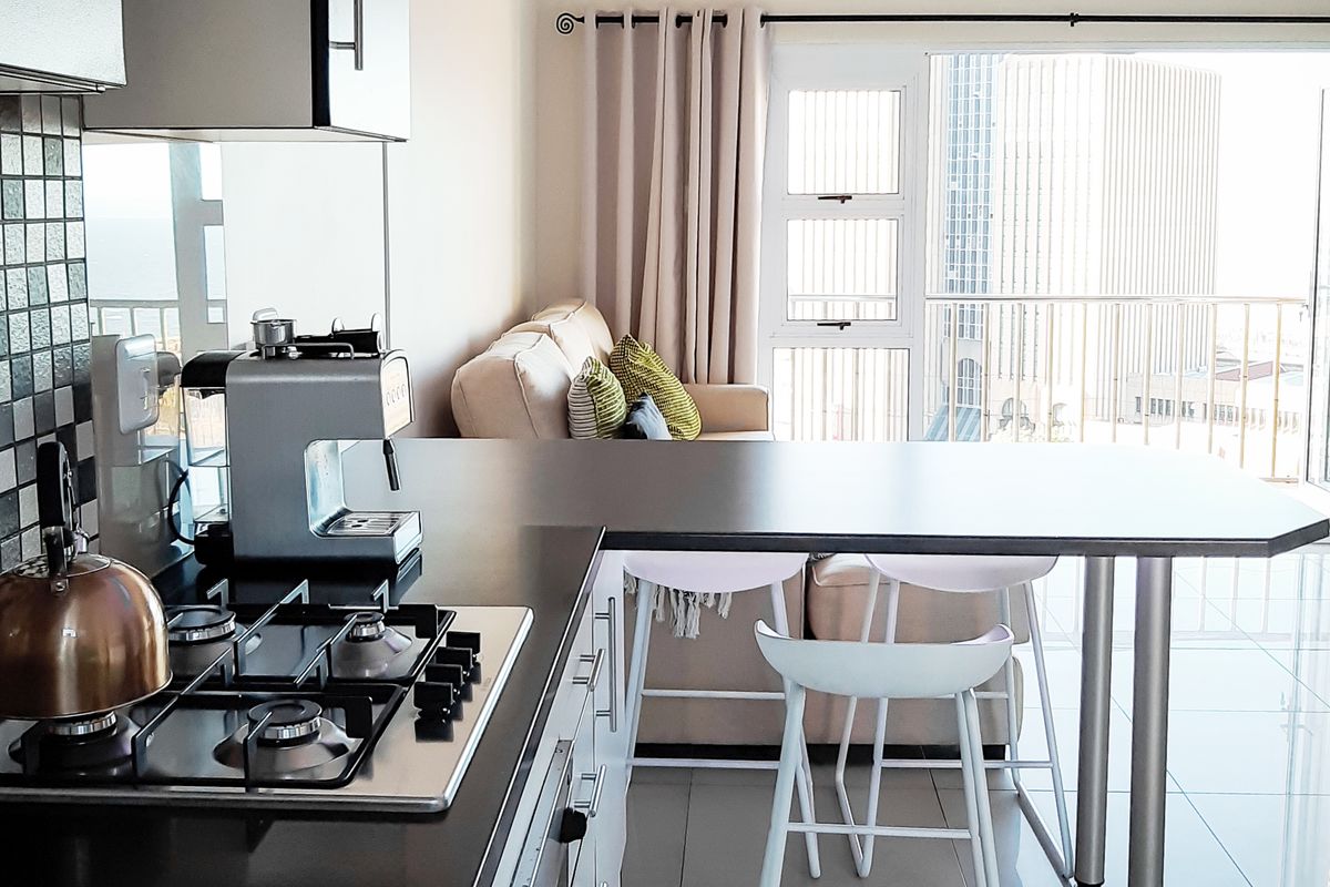 Open plan kitchen featuring a gas hob, extractor fan, and breakfast counter, seamlessly flowing into the living area with balcony access.