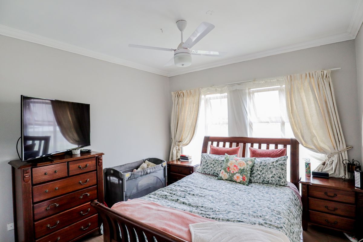 A well-lit bedroom featuring a ceiling fan, neutral wall tones, and large windows with curtain treatments.