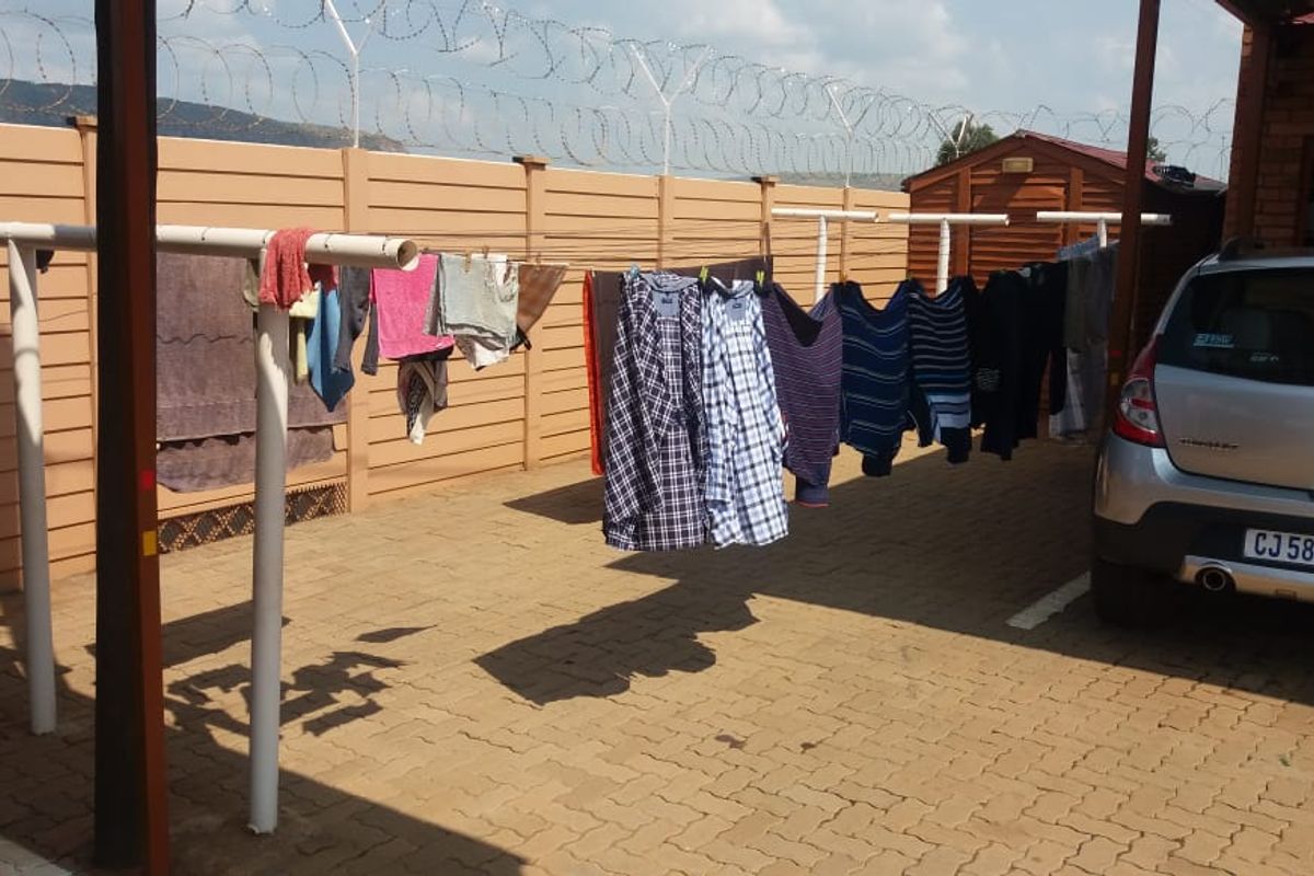 Outdoor paved area featuring a fixed metal washing line structure, enclosed by a perimeter wall with security razor wire.