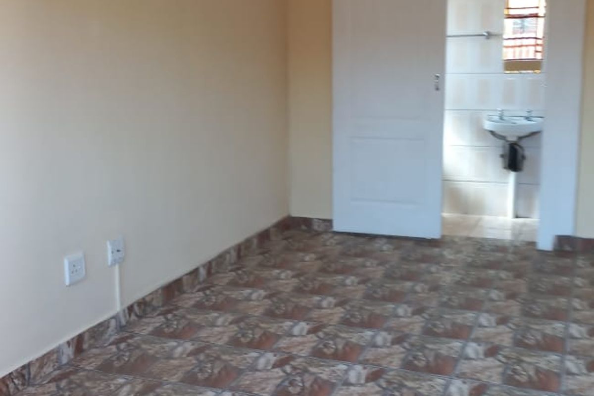 An empty bedroom featuring tiled flooring and a sliding door leading to an en-suite bathroom with a wall-mounted basin.