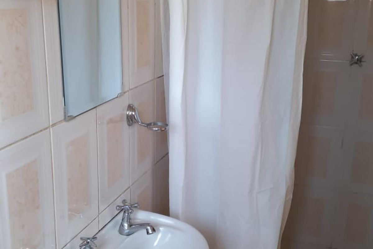 A compact bathroom featuring a wall-mounted basin, shower area with curtain, and tiled walls and flooring.