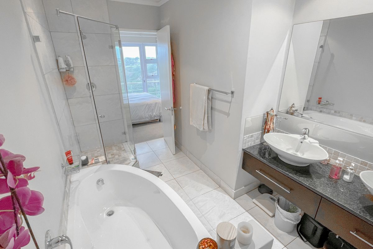 Modern bathroom featuring a double vanity with granite countertop, a separate glass-enclosed shower, and a deep soaking bathtub.
