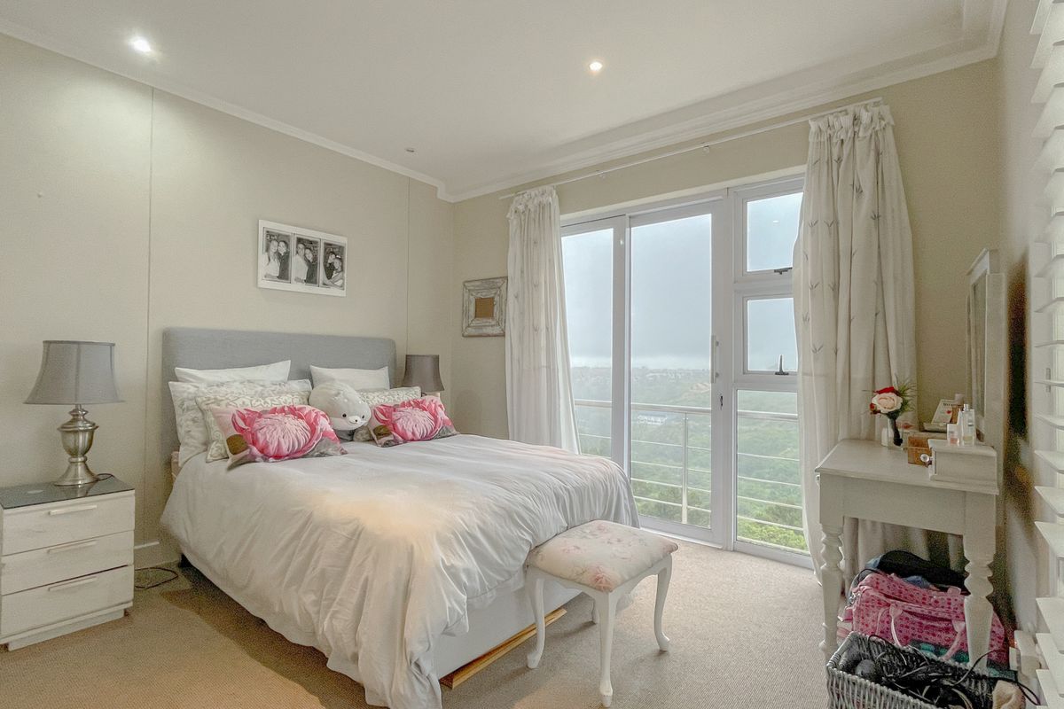 A bright bedroom featuring neutral carpeting, recessed ceiling lighting, and large sliding glass doors that open to a balcony with scenic views.