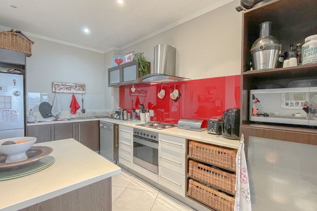 A functional kitchen featuring a red glass splashback, built-in oven, extractor fan, integrated cabinetry, and a central island with stone countertops.