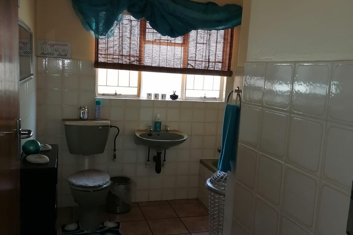 A functional bathroom featuring tiled walls, a wall-mounted basin, and a standard toilet, offering a practical layout with natural light from the window.