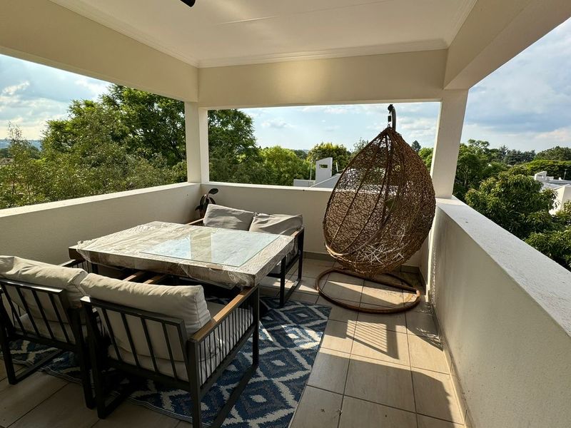 A covered balcony featuring tiled flooring and modern track lighting, offering an open-air space with views of the surrounding greenery.