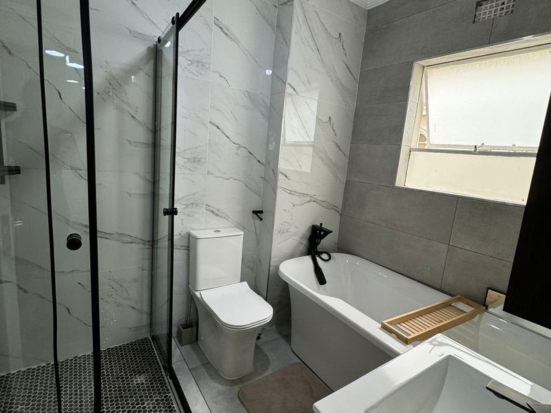Modern bathroom featuring a walk-in shower with black-framed glass, a freestanding bathtub, wall-mounted toilet, and contemporary marble-effect wall tiling.
