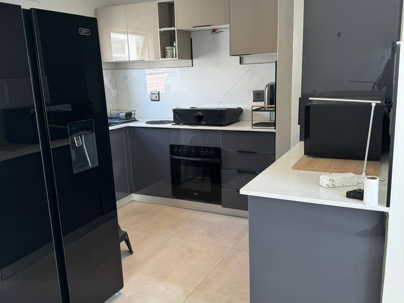 Modern kitchen featuring sleek grey and beige cabinetry, stone countertops, built-in oven, hob, and tiled flooring with contemporary lighting.